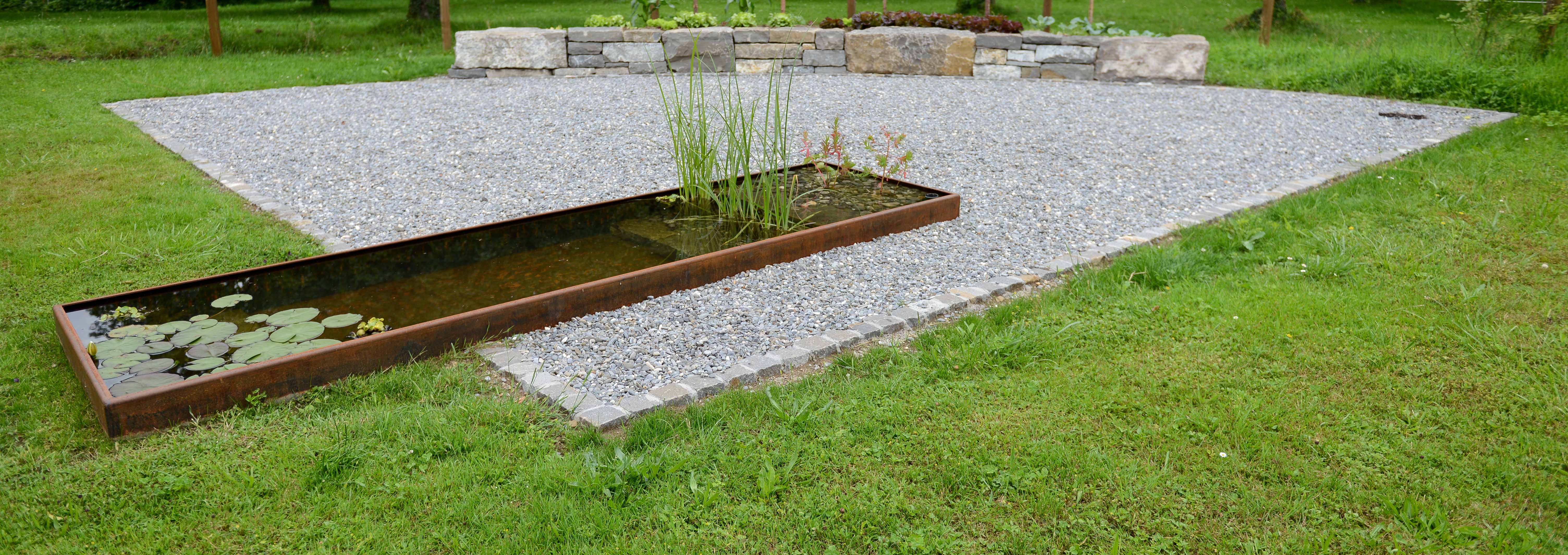 Rechteckiger Teich mit Cortenastahl als Randabschluss auf Rasen und rechteckiger Kiesfläche mit unterschiedlichen Steinabschlüssen