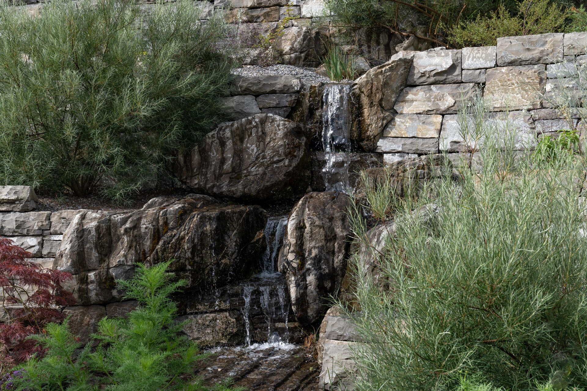 Natursteinmauer: Garten mit Mauern aus Naturstein und dazwischen ein kleiner Wasserfall